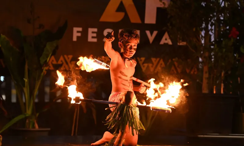 A young Pasifika boy is dancing with fire on a festival stage.