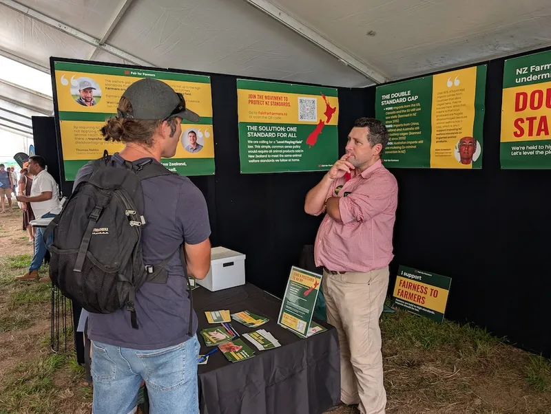 a guy in a red shuirt talks to a passerby with lots of posets around him about animal rights in a marquee with grass on the ground