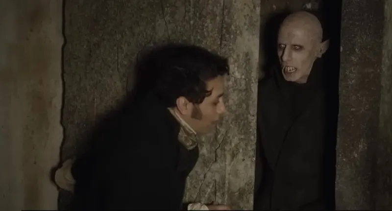 A man in old-fashioned clothing stands near a stone wall, recoiling in fear from a bald, pale figure with sharp teeth and dark sunken eyes emerging from the shadows.