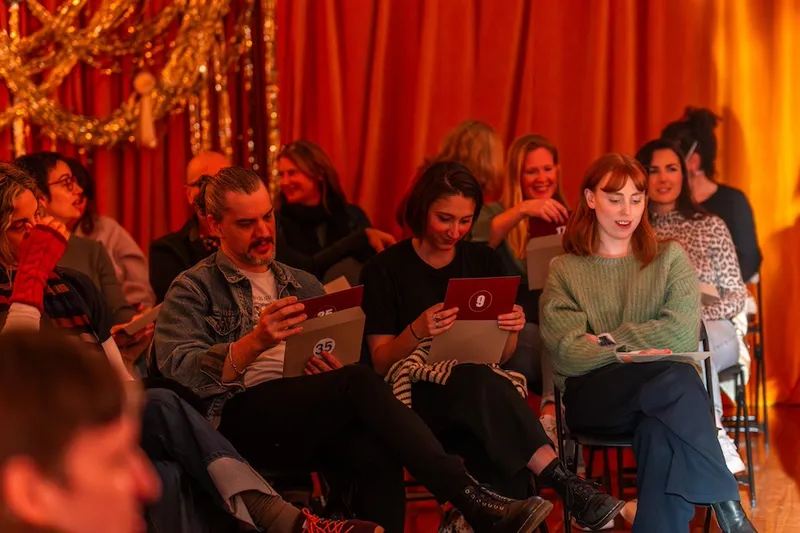 A group of theatre goers sit and open large envelopes with numbers on the outside and a red card on the inside