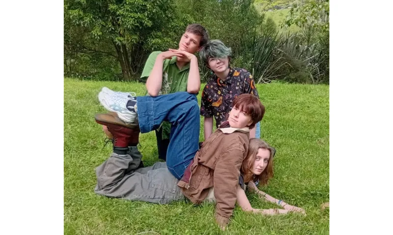 Four high school kids outside on grass, in various poses.