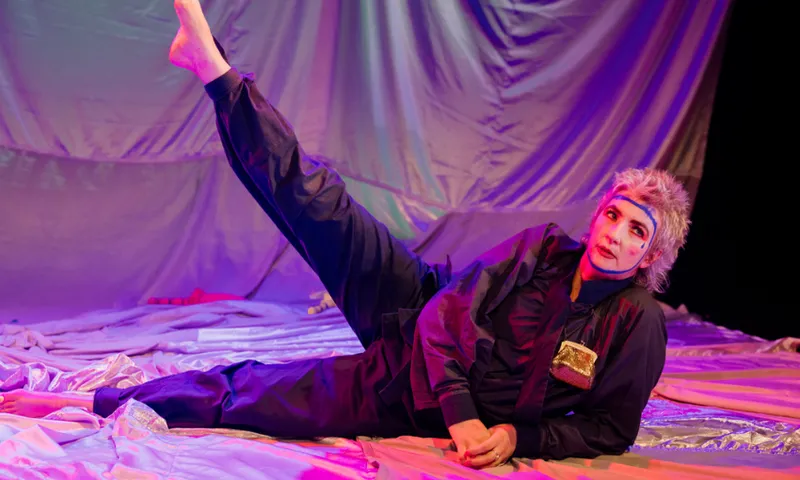 Actor Jo Randerson on stage lying down with one leg up in the air. They are on a large set piece which looks like a huge tent, deflated.