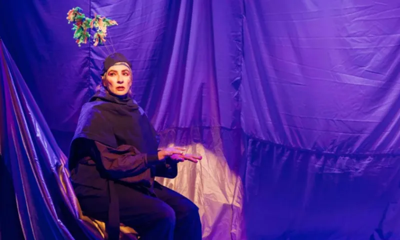 Actor Jo Randerson on stage in costume pretending to type at a desk.