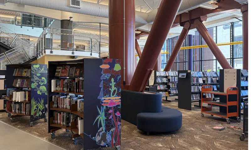 A photo of the inside of Te Matapihi, Wellington's central library showing bookshelves painted with flora and large bolsters.