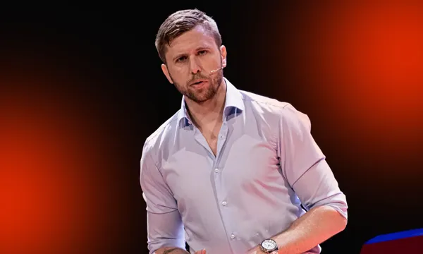 A photo of a young man wearing a button down shirt and in a pose that makes him look like he is about to address an audience.