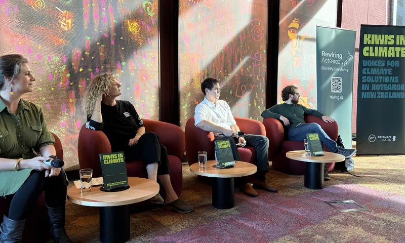 Four people are seated in armchairs each with a little table in front with a book, Kiwis in Climate, and a glass of water. They are panel speakers in an event on climate communication. They are in a beautiful room with painted walls.