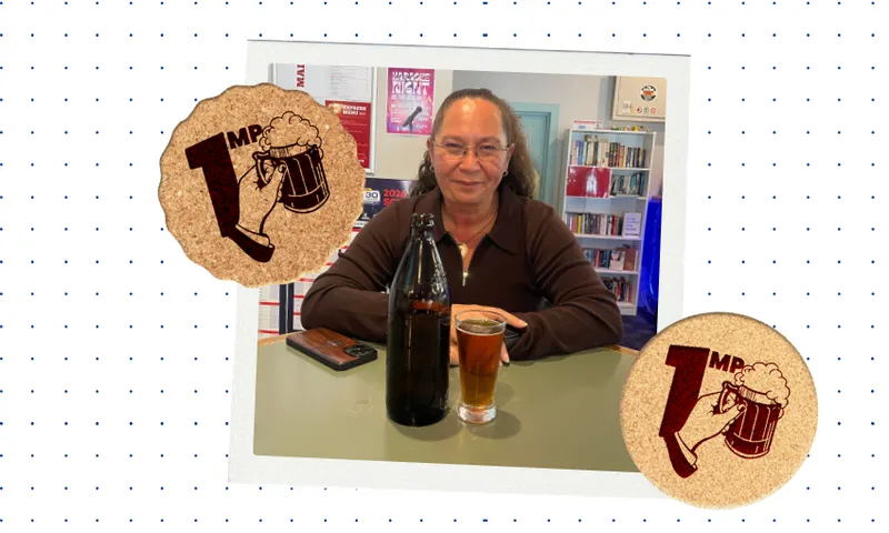 a woman with a slicked back ponytail and glasses sits at a high bar table with a brown beer bottle and pint of beer in front of her. Two stickers with pints of beer are laid over as a template