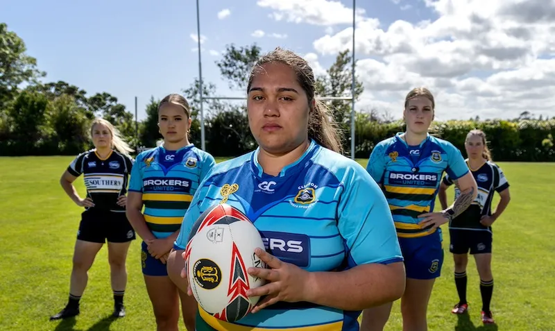 Five women rugby players stand on a rugby field and look at the camera