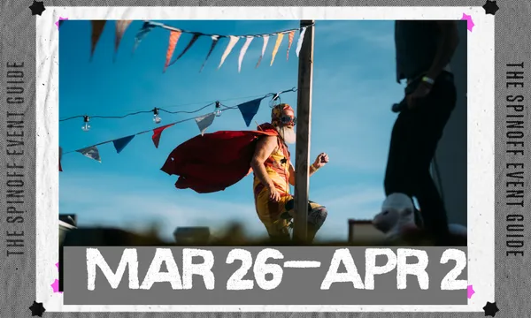 A man on a unicycle wearing wings and a helmet is against a blue sky. There is bunting in the fore and backgrounds.