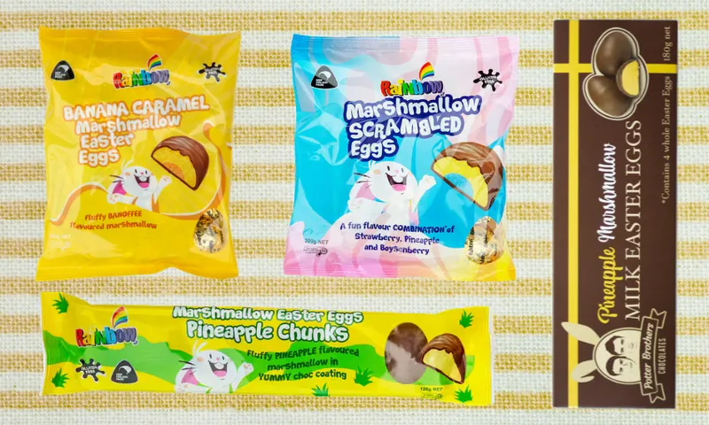 Four colorful packages of Rainbow brand Easter treats on a yellow checkered cloth: banana caramel eggs, marshmallow scrambled eggs, pineapple chunks, and pineapple marshmallow milk chocolate eggs.