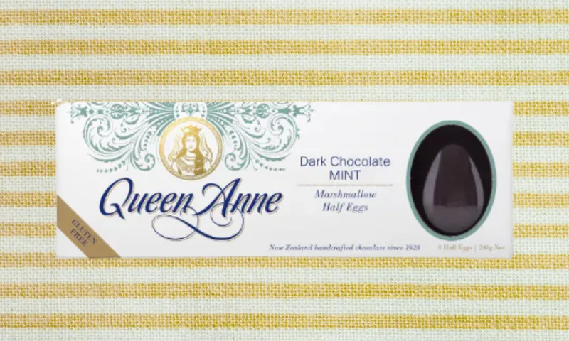 Box of Queen Anne Dark Chocolate Mint Marshmallow Half Eggs on a yellow and white striped background. The box features elegant green designs, a gold logo, and an oval window showing one chocolate half egg.