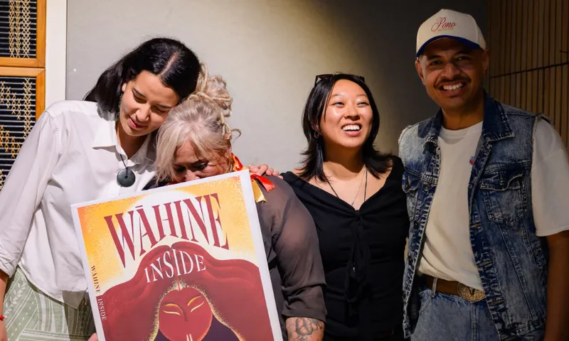 Four people are in a line all in various poses - the image is celebratory and one person is holding a large poster for their project, a book called Wāhine Inside.