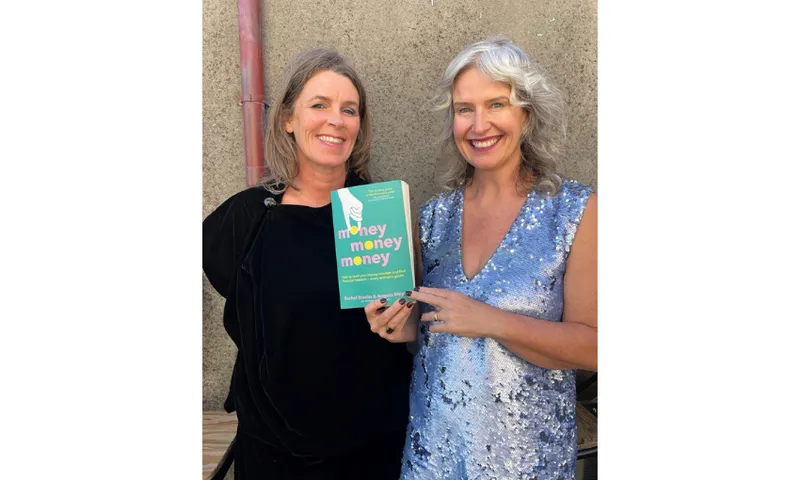 Two middle-aged women standing together and holding a copy of the book they co-authored called Money, Money, Money.