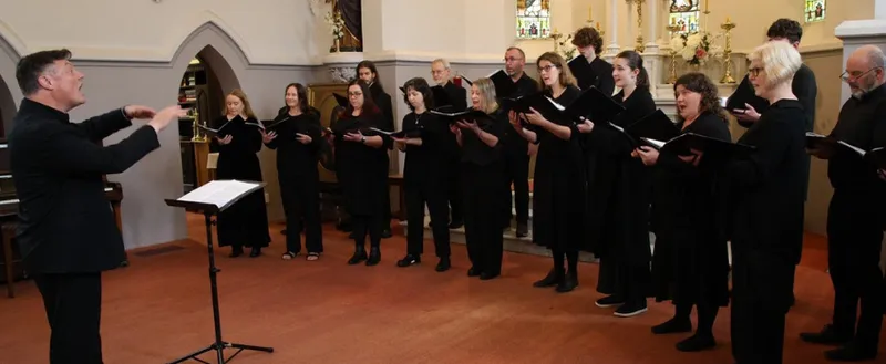 A choir all dressed in black and singing in a church.