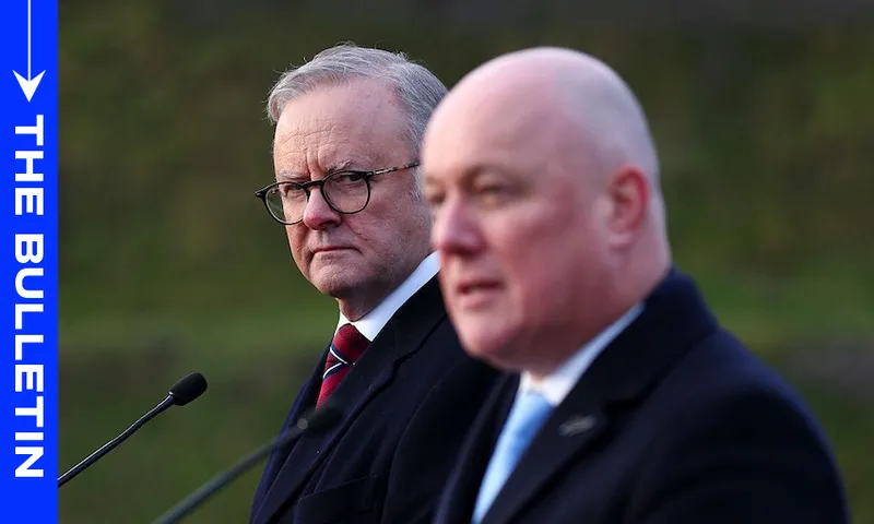 Two men in suits stand at microphones outdoors. The man on the left, wearing glasses, looks intently at the man on the right, who is speaking. A blue vertical sidebar on the left reads "THE BULLETIN.