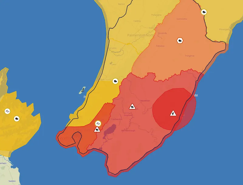 A color-coded map of New Zealand’s lower North Island shows regions in yellow, orange, and red, with warning icons indicating weather alerts. Wellington and surrounding areas are highlighted in red and orange.