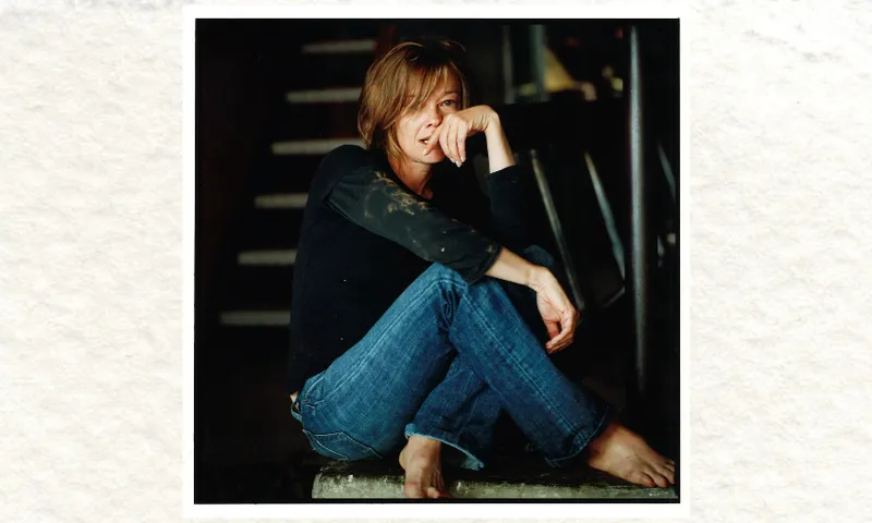A photo of the writer Kelly Ana Morey who is wearing jeans and a black top and is sitting on the floor, her legs folded.