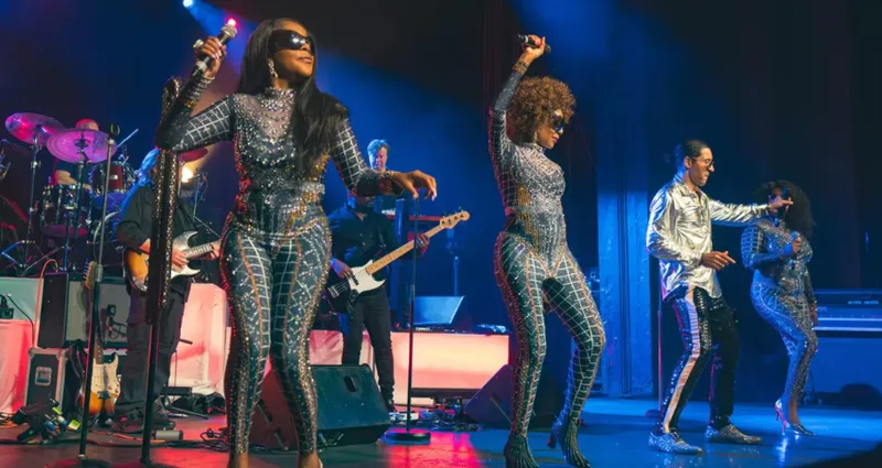 Four musicians on stage - they're wearing glittery body suits.