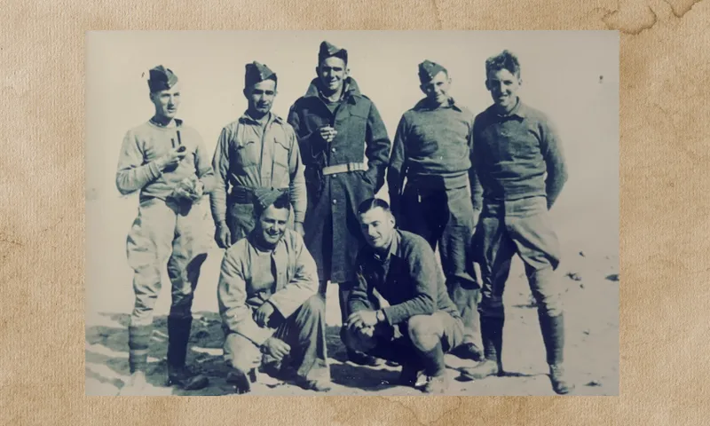 an old photo showing a group of World War 2 army soldiers standing and crouching, smiling at the camera in uniform