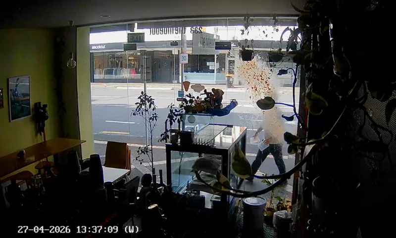 CCTV frame shows the dark inside of a close cafe, with a man in a shirt and pants outside a dirty window holding a plastic container