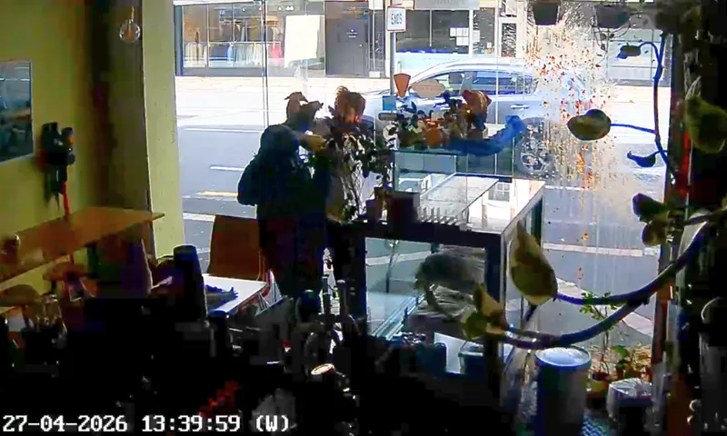 CCTV frame shows the dark inside of a close cafe, with a man in a shirt and pants tussling with a man standing just inside the doorway