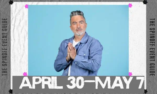 A photo of comedian Dai Henwood wearing a denim shirt with a light blue background behind him. He's looking quizzically at the camera and has his hands in a prayer position.