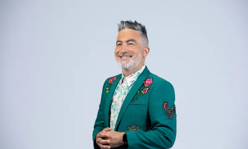 A photo of comedian Dai Henwood, wearing a green suit and smiling.