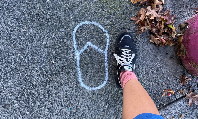 a white painted jandal on the footpath next to a black sneaker