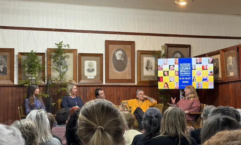 A photo of a panel of writers in an old fashioned hall lined with sepia photos.
