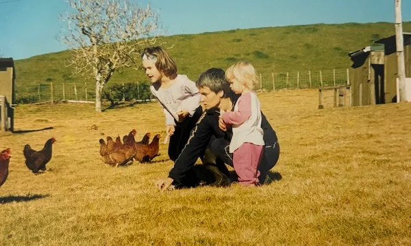 An old family photo showing two young girls standing next to their mum in a field of chickens