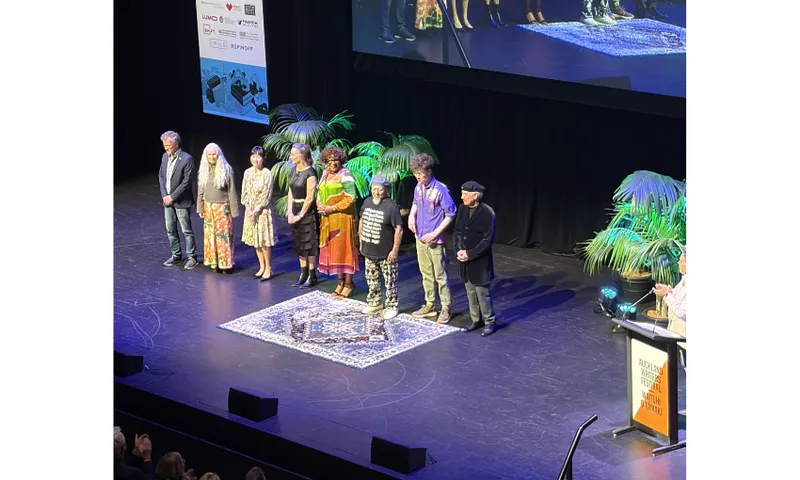 Eight people standing on a large stage with a screen behind them.