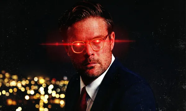 A man in a suit with neatly styled hair is shown at night with a cityscape of blurred lights behind him. His glasses emit bright red laser beams from the lenses, giving a dramatic glowing effect.