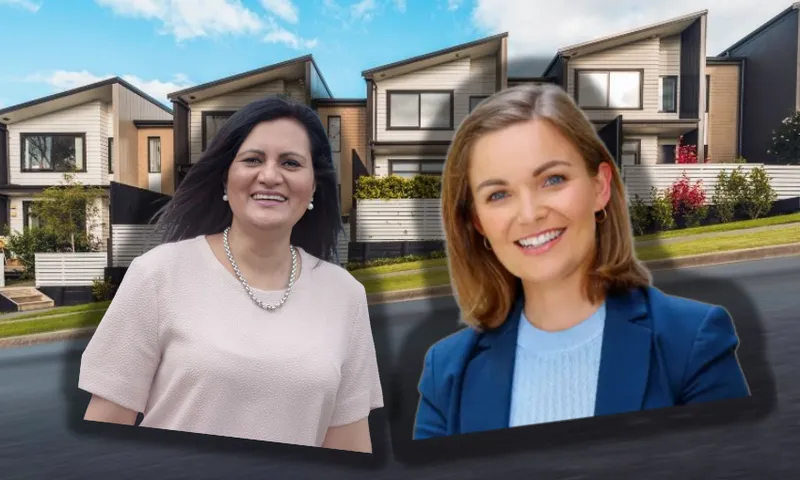 Two smiling women stand in front of modern townhouses on a sunny day. The background shows a row of contemporary homes with blue sky and clouds above.