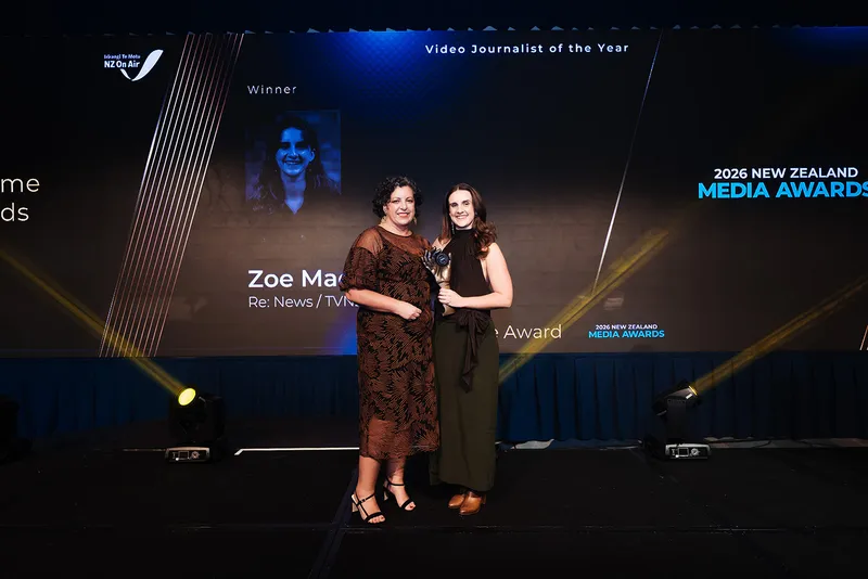 a young woman with long dark hair and wearing a dark dress, poses with an award on a stage