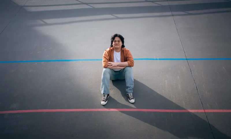 A young man is sitting on a court with his legs folded over his arms looking up at the camera.