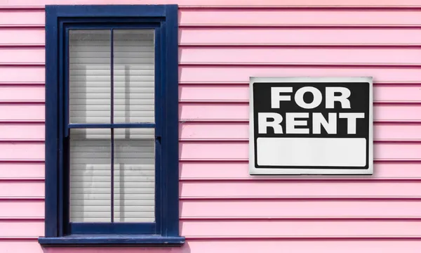 a pink weatherboard home with a dark blue window and a sign saying FOR RENT