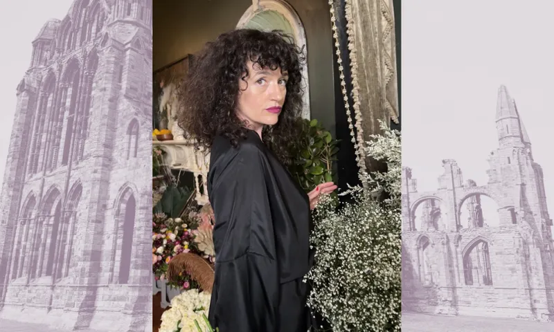 A photograph of Noelle McCarthy who has black curly hair and is wearing black silk. Behind the photo is a faded image of the ruins of Whitby Abbey.