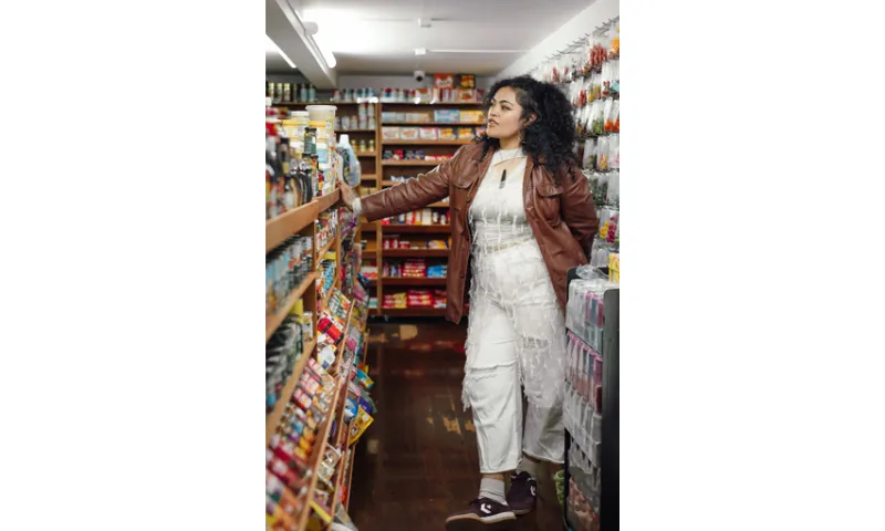 Writer Amber Esau in a supermarket looking at the shelves. She's wearing a white outfit with a brown leather jacket.