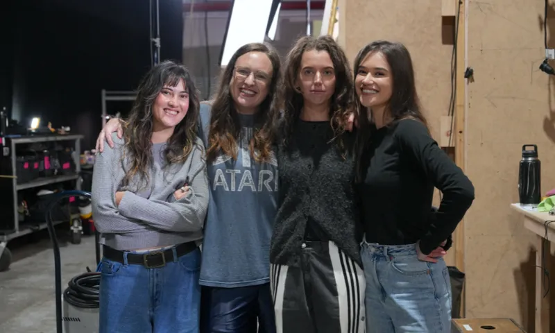 A photo of four young women all standing close and smiling.