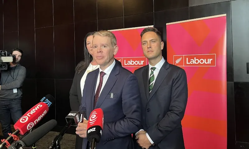 Chris Hipkins stands with Willow Jean Prime and Shanan Halbert in front of Labour Party banners.