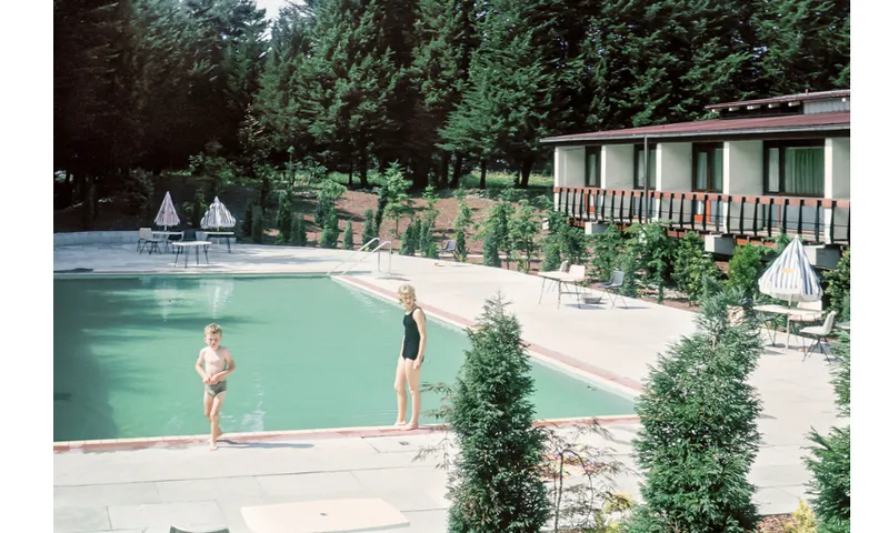 A woman and child stand by a turquoise pool. The image is clearly historic.