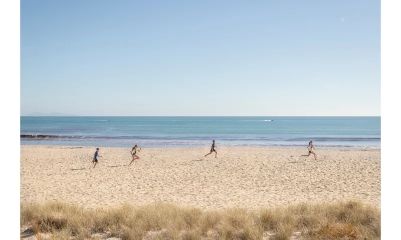 Four figures run across the beach under a pale blue sky.