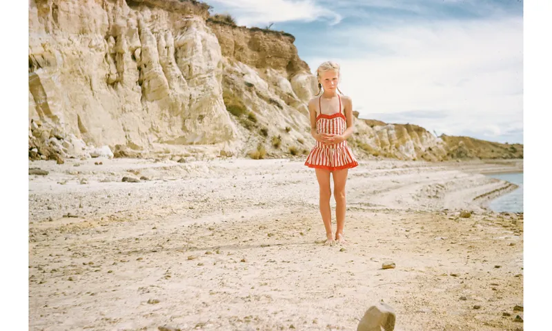 A young girl in a red and cream striped bathing suit is standing on the beach.