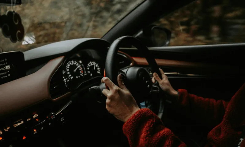 A photo of a wheel of a car with two hands on it.
