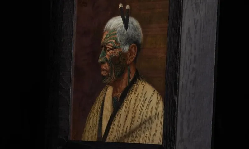 A framed portrait of an older person in profile, featuring facial tattoos and two feathers in their hair, wearing a robe with dark stripes, set against a dark background.