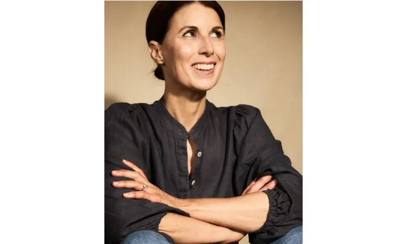 A photo of Meg Mason who is a middle aged woman with brown hair tied up. She is smiling and glancing up to her left.