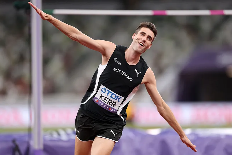 a tall, skinny man wears a black singlet and shorts and runs, smiling, with his arms spread like wings
