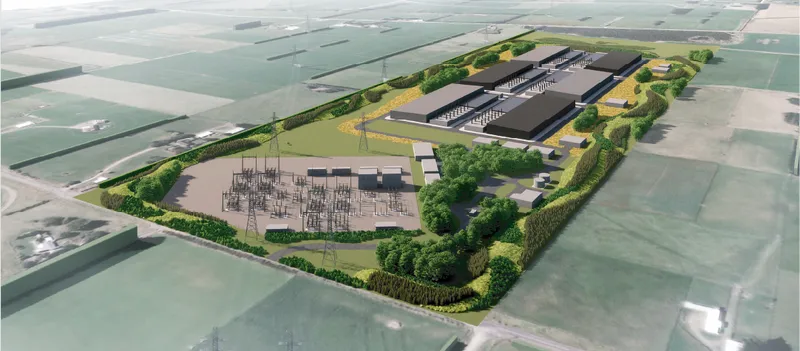 Aerial view of a large industrial complex surrounded by green fields and trees, featuring several rectangular buildings and an electrical substation within a fenced perimeter.