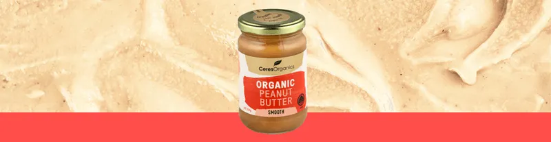A jar of Ceres Organics Smooth Organic Peanut Butter with a gold lid is shown against a background of creamy peanut butter.