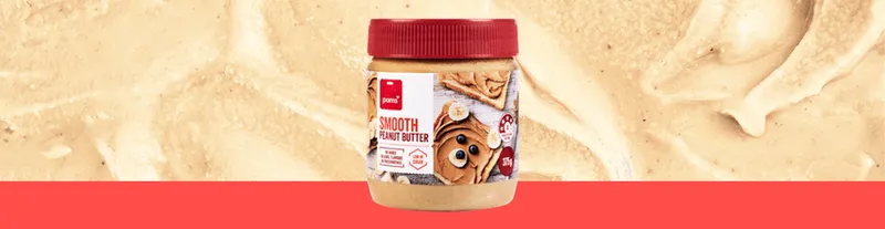 A jar of smooth peanut butter with a red lid sits in front of a creamy peanut butter background and a red stripe along the bottom. The label features toast topped with peanut butter and banana slices.